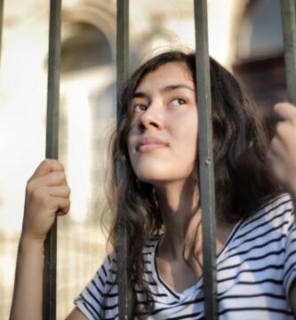 sad isolated young woman looking away through fence with hope