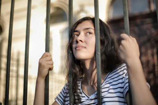 sad isolated young woman looking away through fence with hope
