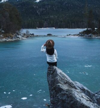 man in white shirt and black pants sitting on rock near lake